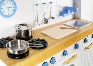 Leomark Cucina Saint Tropez in legno bianco blu, cucina con accessori, orologio, forno, lavatrice e lavastoviglie + 4 quattro casse di legno con generi alimentari, Dimensioni: 106x32x107 cm.